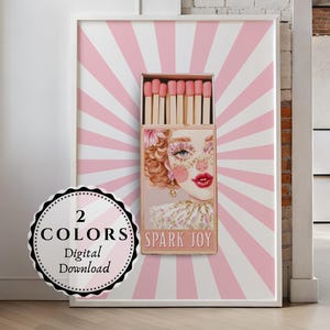 以下が含まれることがあります： 女性の顔と「SPARK JOY」の文字が入ったマッチ箱のデザインの額入りプリント。背景はピンクと白のストライプです。「2 COLORS Digital Download」と書かれた丸いステッカーが付いています。