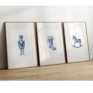 Puede incluir: Tres impresiones enmarcadas con un diseño de porcelana azul y blanco. Las impresiones representan un cascanueces, una bota con flores y un caballo de balancín.