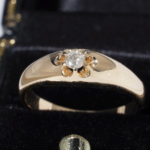 May include: A gold ring with a flower design. The ring features a central diamond surrounded by six gold petals. The band is smooth and polished, and the ring is set against a black background.