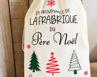 May include: A cream-coloured fabric drawstring gift bag featuring red and green Christmas tree graphics, red snowflakes, and black and red text that reads: EN PROVENANCE DE LA FRABRIQUE DU Père Noël, Livraison spéciale pour LOLO.