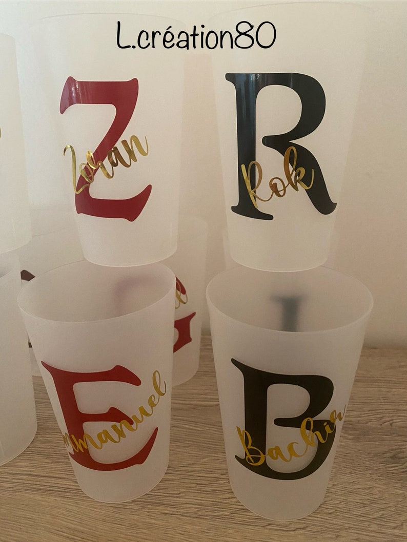 May include: Four clear plastic cups with red and black letters and gold lettering. The letters are Z, R, E, and B. The names on the cups are "Zoran", "Rok", "Emmanuel", and "Bachir".