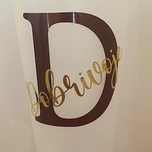 May include: A white plastic cup with a brown letter D and the word "Dobrivoje" written in gold cursive lettering.
