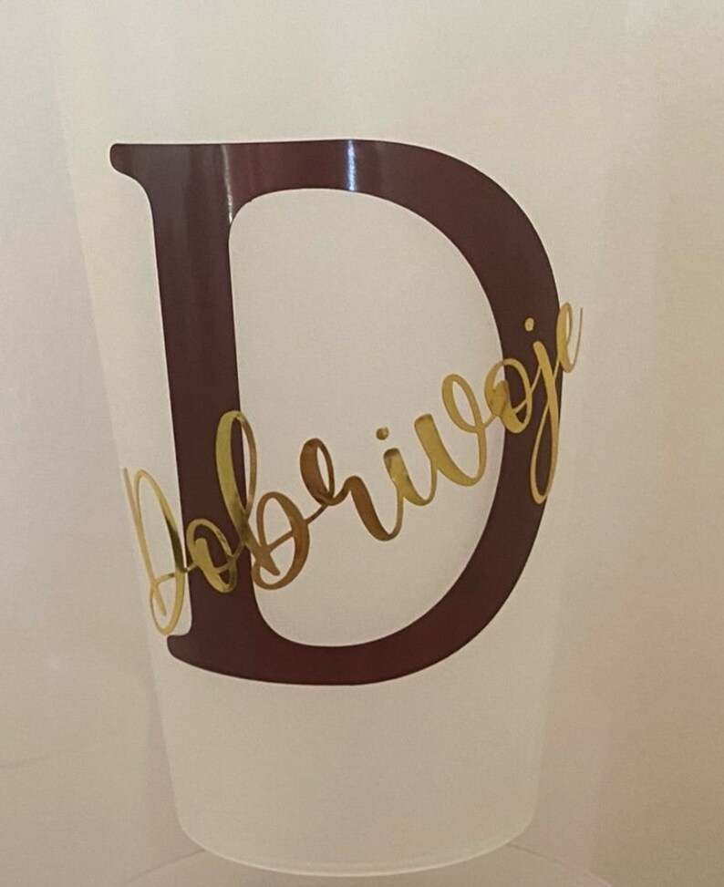 May include: A white plastic cup with a brown letter D and the word "Dobrivoje" written in gold cursive lettering.