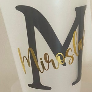 May include: A white plastic cup with a black letter "M" and the name "Miroslav" written in gold cursive lettering.