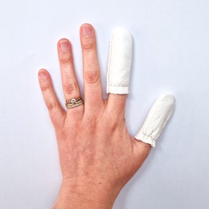 May include: A hand wearing two white fingertip protectors, one on the index finger and one on the middle finger. The hand is also wearing a gold ring with a small clear stone.