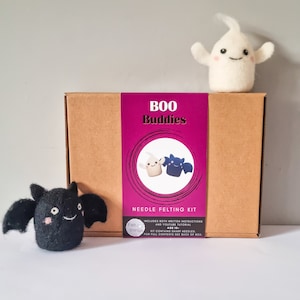 May include: A brown cardboard box for a Boo Buddies needle felting kit with a purple label featuring the text Boo Buddies and Needle Felting Kit. A white felt ghost sits on top of the box, and a black felt bat sits to the left of the box.