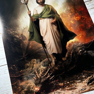 May include: A painting of a man in a white robe and green cloak standing on a dragon. The man is holding a staff with a white flower on top. The dragon is lying on the ground with its head facing the viewer. The background is a fiery orange and yellow.