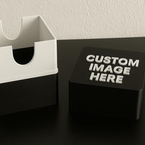 Può includere: Un porta carte bianco e nero e una scatola nera con la scritta "CUSTOM IMAGE HERE" in bianco. Il porta carte è bianco sopra e nero sotto. La scatola è rettangolare.