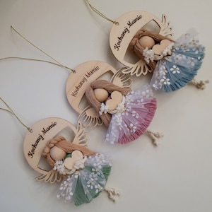 Peut inclure: Trois ornements d'ange en bois avec une ficelle dorée pour accrocher. Chaque ange a une jupe en tulle de couleur différente et une tête en bois avec des cheveux en laine brune. Les ornements sont inscrits avec le texte "Kochanej Mamie" qui se traduit par "Maman bien-aimée".