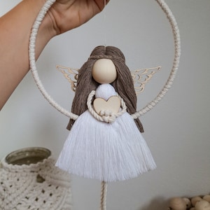 Peut inclure: Une poupée ange blanche et brune avec des ailes, tenant un cœur, suspendue à un cercle de corde blanche.