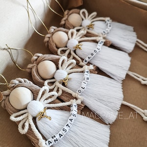 Può includere: Quattro ornamenti di angelo in macramè fatti a mano con frange bianche e perline di legno. Ogni ornamento ha un nome scritto in lettere dorate: Olivia, Karolina, Anastasia e Oliwia.