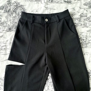 May include: Black pants with a single leg slit on the left side. The pants have a straight leg and a high waist.