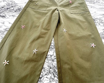 Könnte beinhalten: Olivengrüne weite Hose mit gestickten Blumen in Rosa, Weiß und Grün.