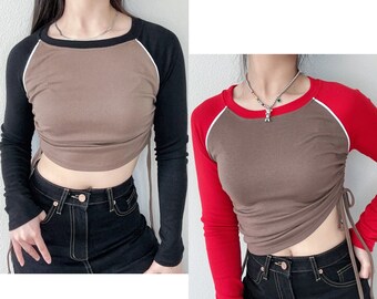 May include: Two long-sleeved shirts with brown, black, and red color blocking. The shirts have a white trim around the neck and sleeves. The shirts are cropped and have a drawstring at the side.