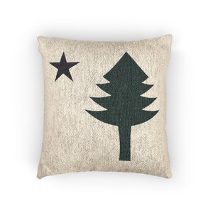 May include: A square throw cushion with a textured beige fabric base. The front features a dark green pine tree silhouette positioned on the right side and a dark green five-pointed star located in the upper left corner of the cushion cover.