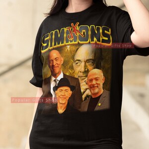 Puede incluir: Camiseta negra con un gráfico amarillo de la palabra "Simpsons" con una X roja. El gráfico también presenta cuatro caras de hombres, incluido un hombre con un sombrero negro.