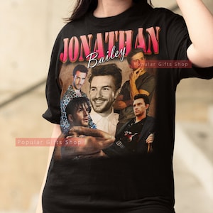 May include: Black t-shirt with a collage of photos of Jonathan Bailey, a British actor. The shirt has the text "JONATHAN Bailey" in pink and red letters. The text "Popular Gifts Shop" appears twice on the shirt.
