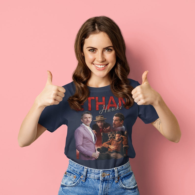 May include: A woman wearing a navy blue t-shirt with a vintage-style graphic of Ethan Hawke. The graphic features multiple images of Ethan Hawke in different roles. The t-shirt has the text "Ethan Hawke" in red lettering.