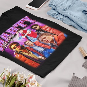 Puede incluir: Camiseta negra con un gr&aacute;fico morado y blanco del texto "Marty McFly" y un grupo de personas con chaquetas rojas.