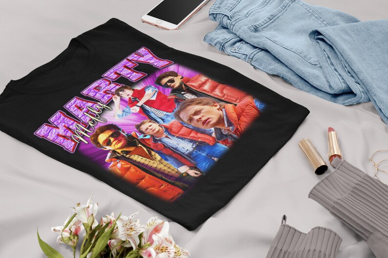 Puede incluir: Camiseta negra con un gr&aacute;fico morado y blanco del texto "Marty McFly" y un grupo de personas con chaquetas rojas.