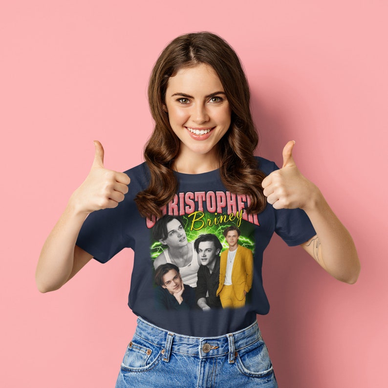May include: A navy blue t-shirt with a vintage-style graphic featuring three men's faces and the text "Christopher Briney" in pink and yellow letters.