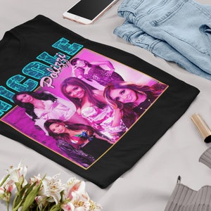 May include: Black t-shirt with a retro-style graphic of the girl group "Nicole Polizzi" in a pink and blue color scheme.