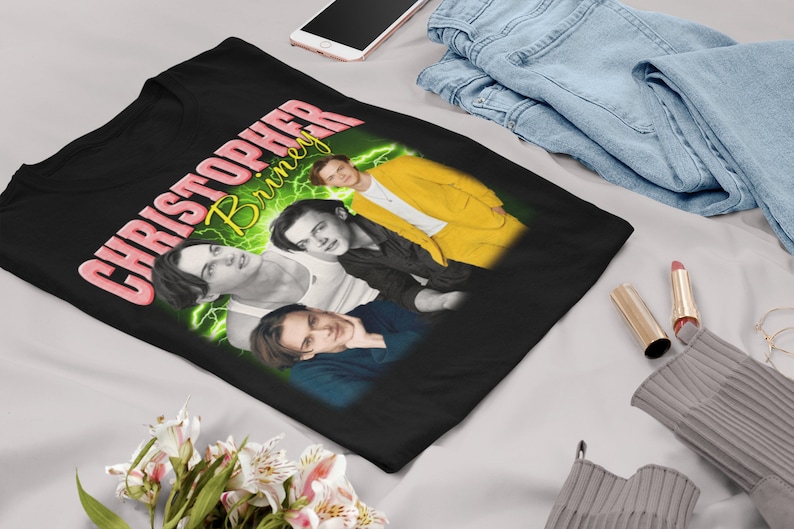 May include: Black t-shirt with a graphic print of a man's face with the text "CHRISTOPHER BRINLEY" in pink and yellow.