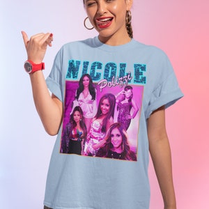 May include: A light blue t-shirt with a graphic print of a collage of women's faces and the text "Nicole Polizzi" in pink and blue letters.