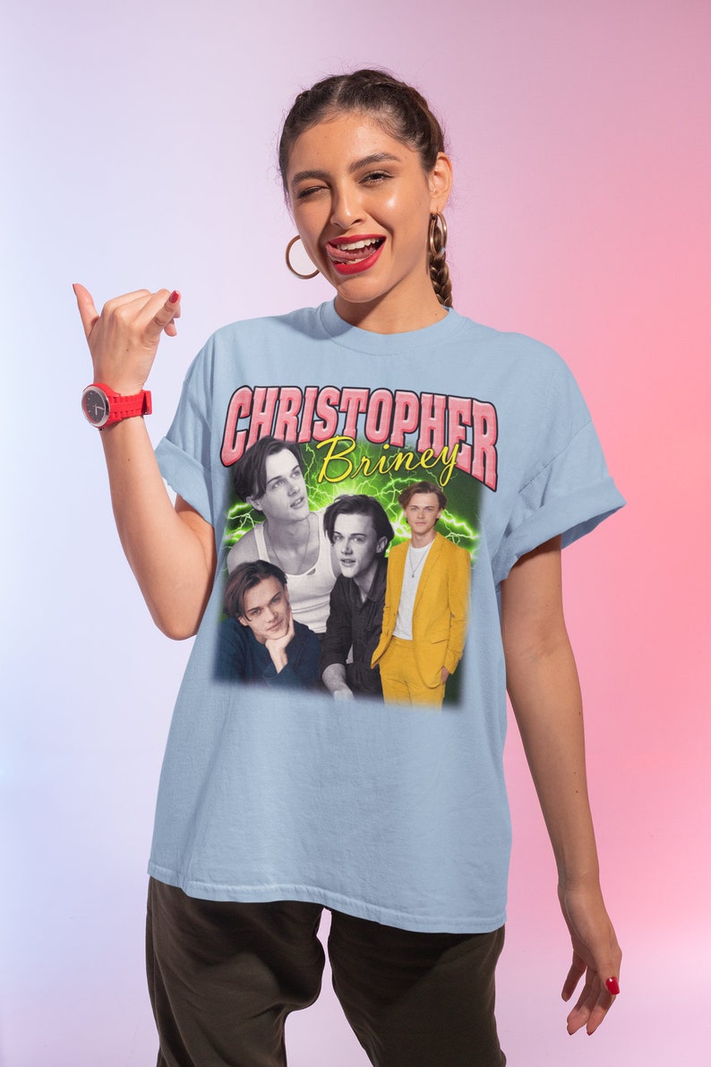 May include: Light blue t-shirt with a graphic print of a collage of four photos of Christopher Briney. The text "CHRISTOPHER Briney" is printed in pink letters above the photos.