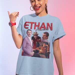 May include: A light blue t-shirt with a graphic print of Ethan Hawke in red text. The graphic features four different images of Ethan Hawke from different movies.