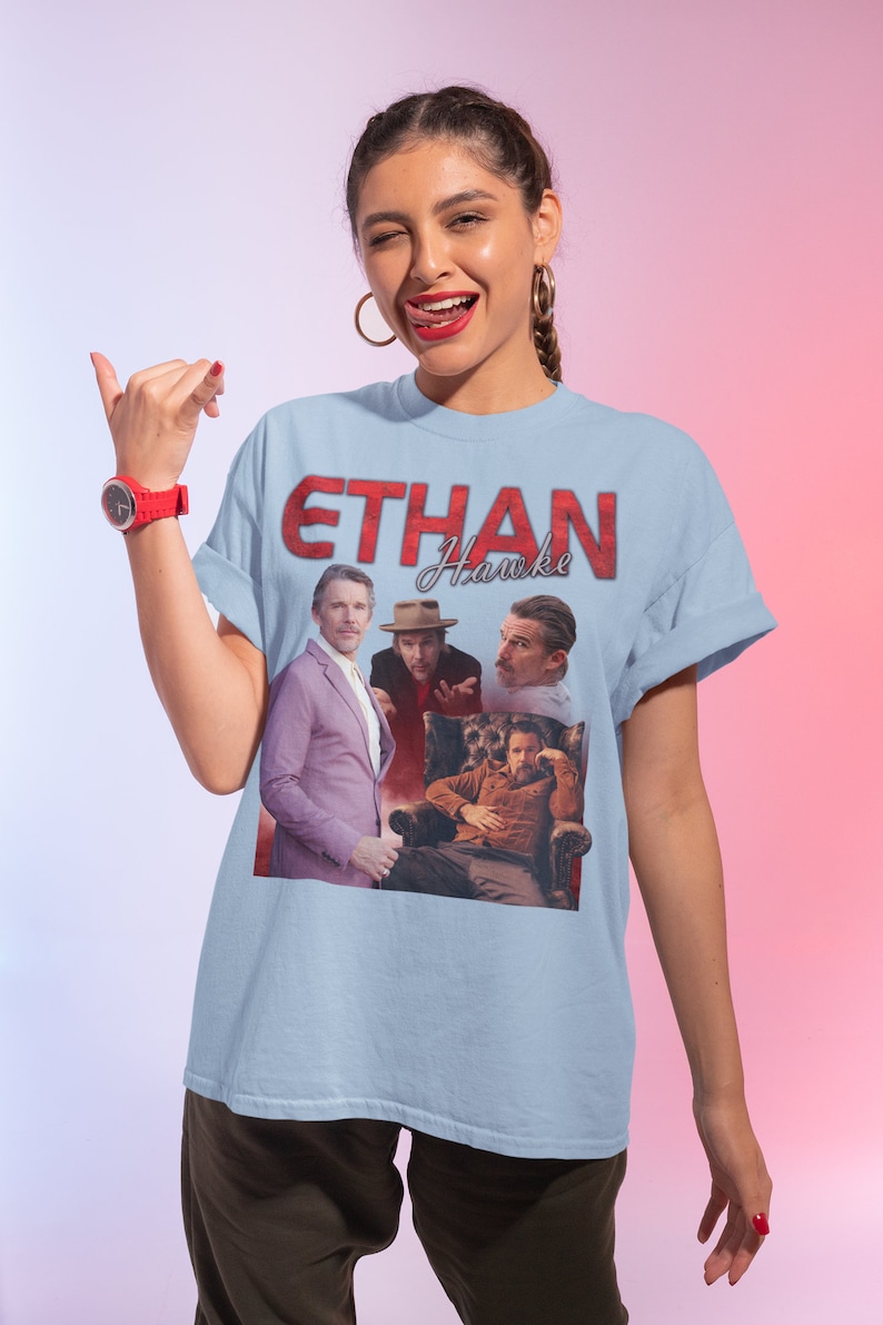 May include: A light blue t-shirt with a graphic print of Ethan Hawke in red text. The graphic features four different images of Ethan Hawke from different movies.