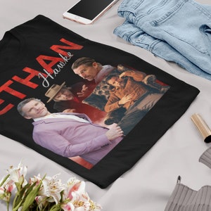 May include: Black t-shirt with a red graphic that says "ETHAN HAWKE" in a bold font. The graphic also features three images of Ethan Hawke in different poses.