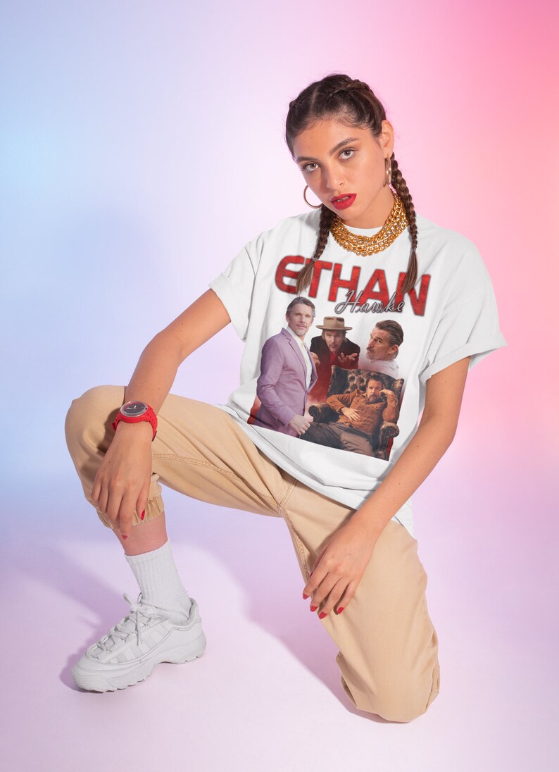May include: A white t-shirt with a red graphic print of Ethan Hawke. The graphic features a collage of four images of Ethan Hawke in different poses. The text "Ethan Hawke" is printed in red letters above the collage.