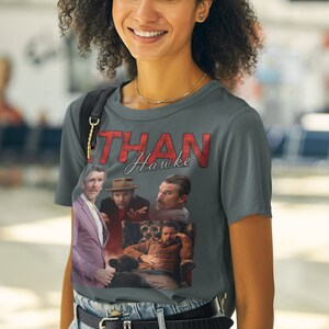 May include: A gray t-shirt with a collage of images of Ethan Hawke. The text "Ethan Hawke" is printed in red on the shirt.