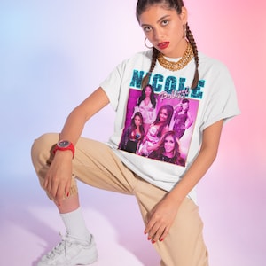 May include: A white t-shirt with a graphic print of a group of women with the text "Nicole Polizzi" in blue and pink.