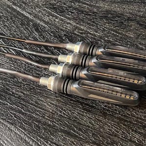 May include: A set of four black motorcycle turn signals with clear lenses and red tips. The turn signals have a sleek, modern design and are arranged on a textured surface.