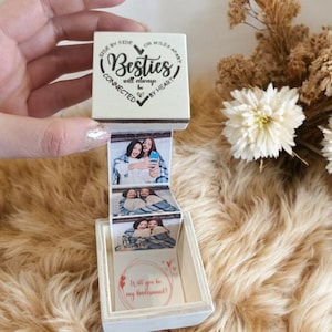 May include: A white wooden box with a heart-shaped design and the text "Besties will always be connected by heart" on the top. The box opens to reveal a series of photos and a message that says "Will you be my bridesmaid?"