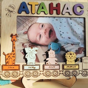 May include: Wooden photo frame with the name "ATAHAC" in colorful letters. The frame features a baby's photo, along with decorative animal cutouts and a train design. Includes baby's birth details: 31cm, 3430g, 22:27, and 19.09.22.
