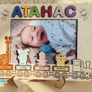 May include: Wooden photo frame with the name "ATAHAC" in colorful letters. The frame features a photo of a baby and decorative animal cutouts. Includes baby's birth details: 51cm, 3410g, 22:27, and 19.09.22.