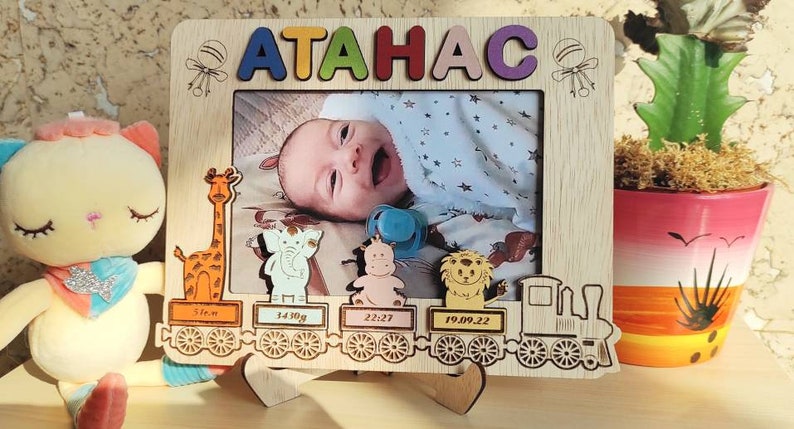 May include: Wooden photo frame with the name "ATAHAC" in colorful letters. The frame features a photo of a baby and decorative animal cutouts. Includes baby's birth details: 51cm, 3410g, 22:27, and 19.09.22.