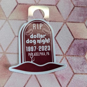 May include: A brown and white sticker shaped like a tombstone with the text "RIP dollar dog night 1997-2023 PHILADELPHIA, PA".