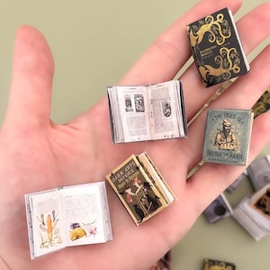 Peut inclure: Plusieurs petits livres miniatures, dont certains ouverts, sont tenus dans une main. Les livres ont des couvertures détaillées avec des motifs dorés et noirs, et les livres ouverts affichent des pages imprimées. Un livre est intitulé "The Tales of Beedle the Bard."