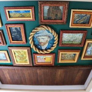 May include: A green wall with a wooden frame surrounding a collection of framed artwork. The artwork includes paintings of landscapes, portraits, and still lifes. The frames are all different sizes and shapes, and they are arranged in a random pattern.