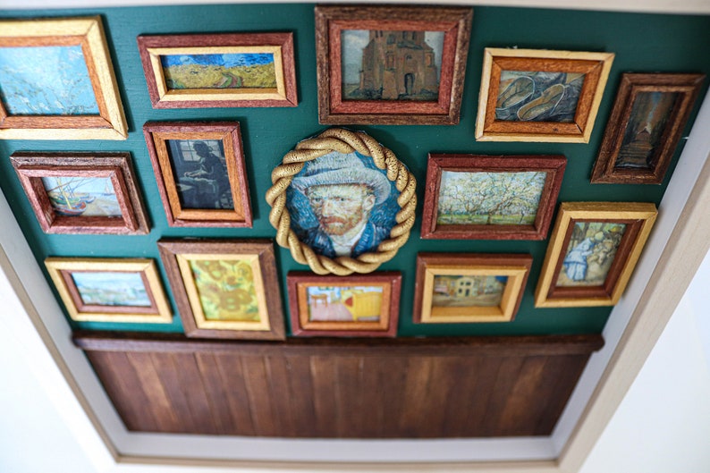 May include: A green wall with a wooden frame surrounding a collection of framed artwork. The artwork includes paintings of landscapes, portraits, and still lifes. The frames are all different sizes and shapes, and they are arranged in a random pattern.
