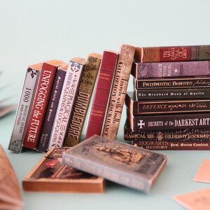 May include: A collection of miniature books with titles like "Unfogging the Future" and "Fantastic Beasts." The books are in various colors, including red, burgundy, and brown, and are stacked and leaning against each other.