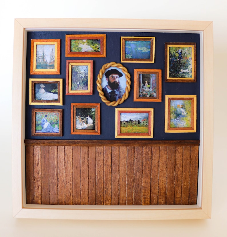 May include: A miniature wooden wall display with a dark blue background and a wood-paneled lower section. The wall is decorated with 11 framed pictures, including a portrait of a man with a beard, landscapes, and still lifes.