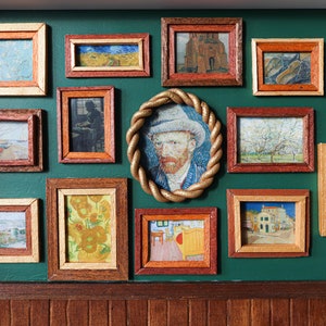May include: A green wall with a collection of framed artwork, including a self-portrait of Vincent van Gogh, landscapes, and still lifes.