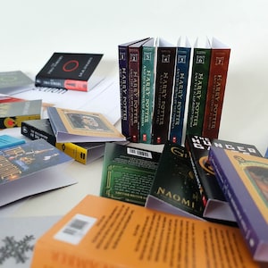 Peut inclure: Une collection de livres broch&eacute;s, dont la s&eacute;rie Harry Potter, Le Hobbit et Hunger Games. Les livres sont dispos&eacute;s en pile et sur une surface blanche.