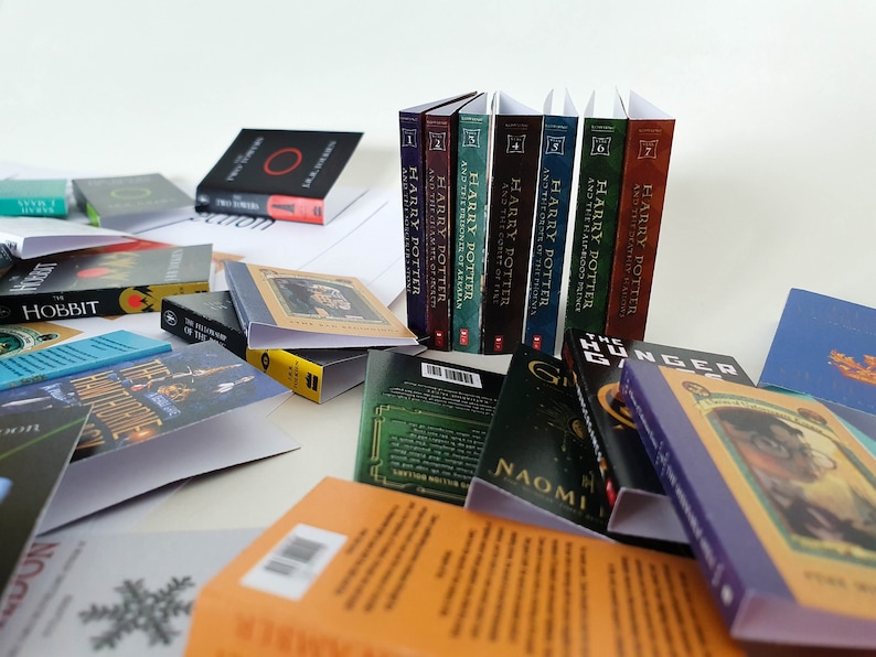 Peut inclure: Une collection de livres broch&eacute;s, dont la s&eacute;rie Harry Potter, Le Hobbit et Hunger Games. Les livres sont dispos&eacute;s en pile et sur une surface blanche.