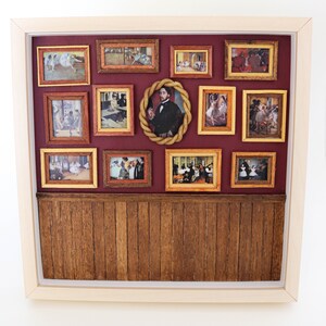 May include: A miniature dollhouse room with a burgundy wall and a wood-paneled floor. The wall is decorated with 12 framed pictures of dancers and a portrait of a man.